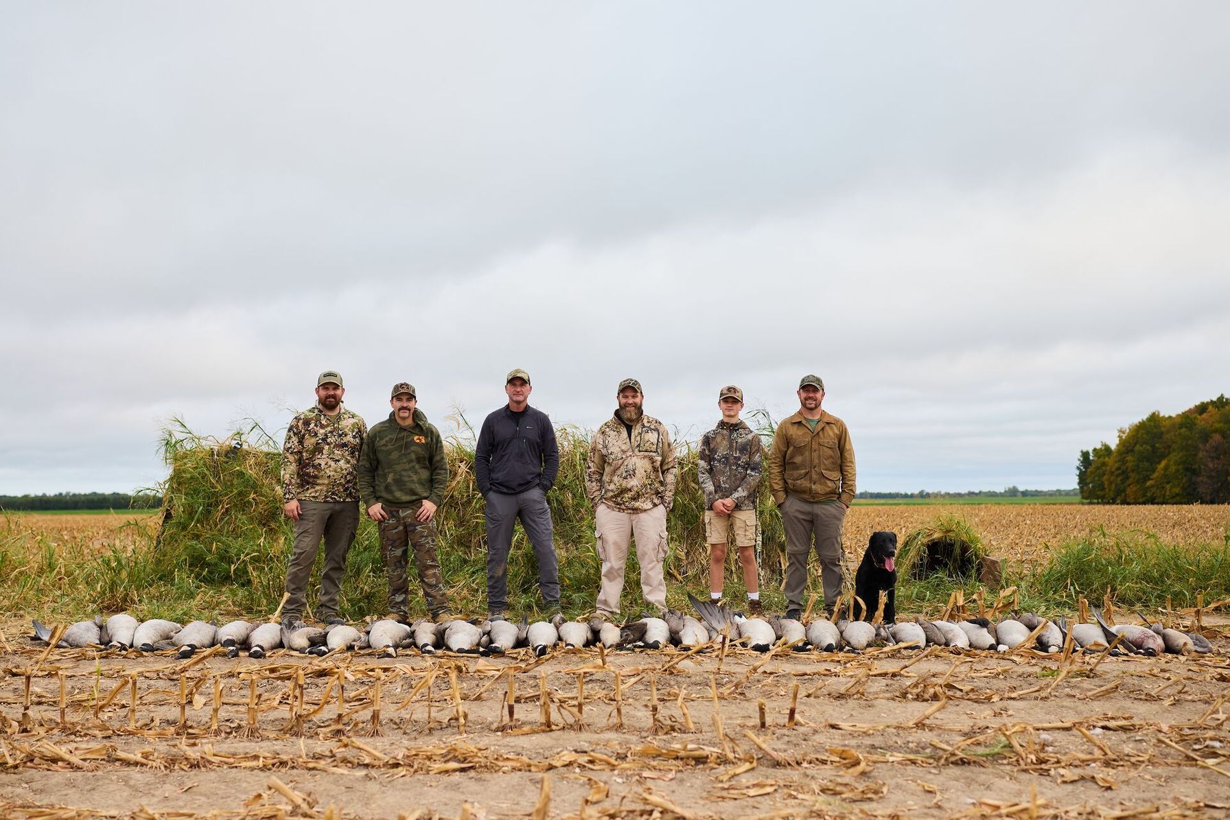 Group of hunters stand behind line of geese after hunt, Kansas waterfowl hunting land concept.