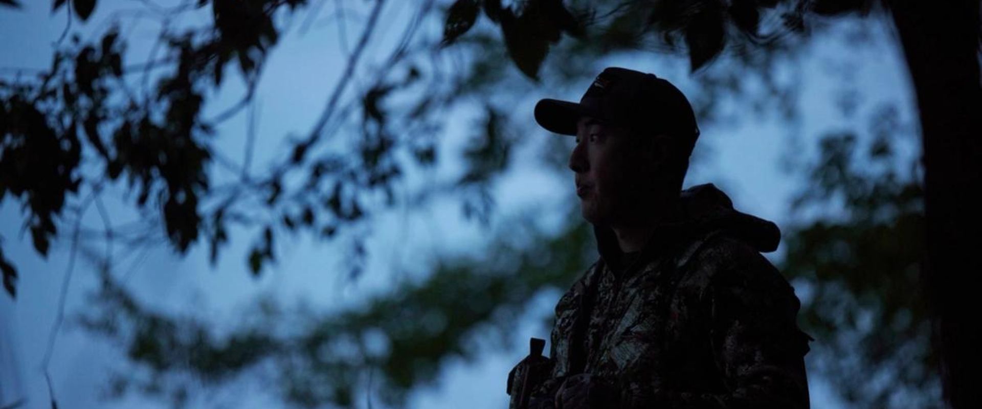 A hunter stands near a tree in the dark, night hunting concept.