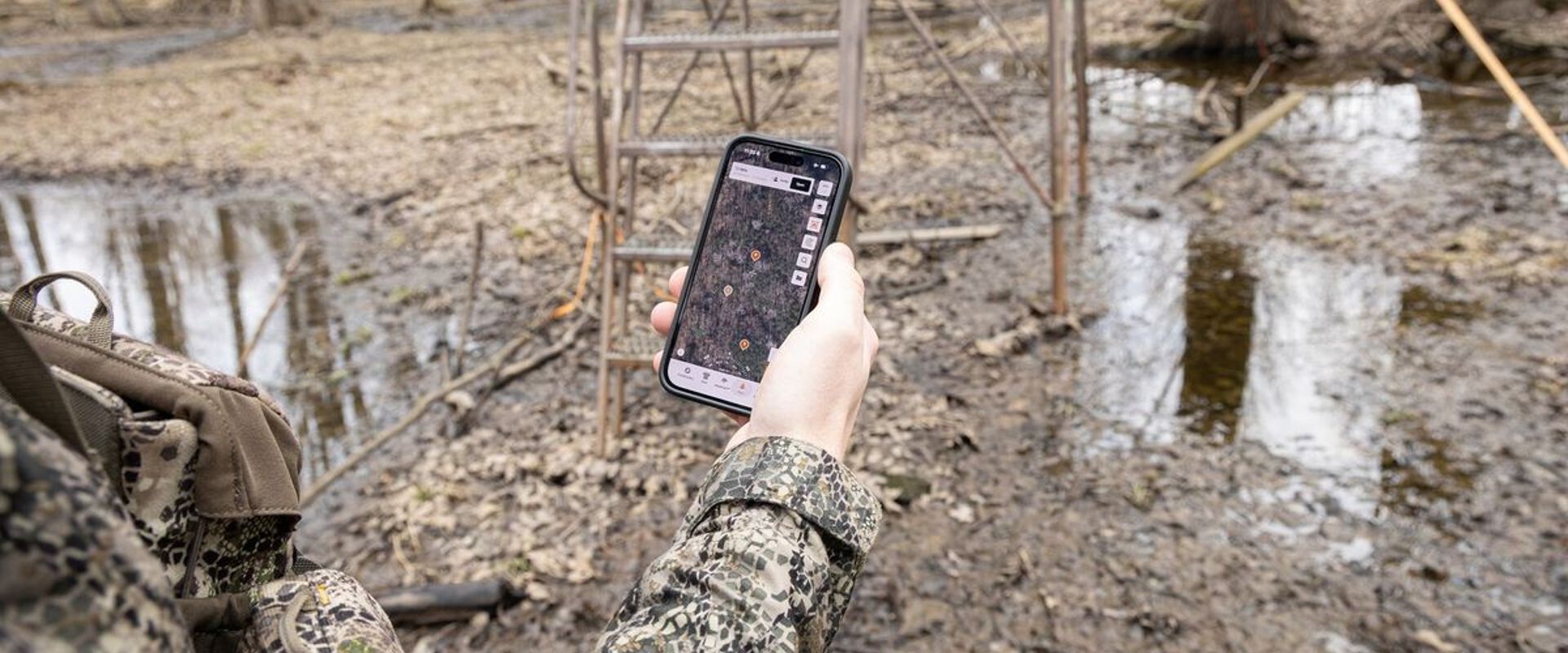 Hand holding phone showing HuntWise near stand, find property lines for hunting concept.