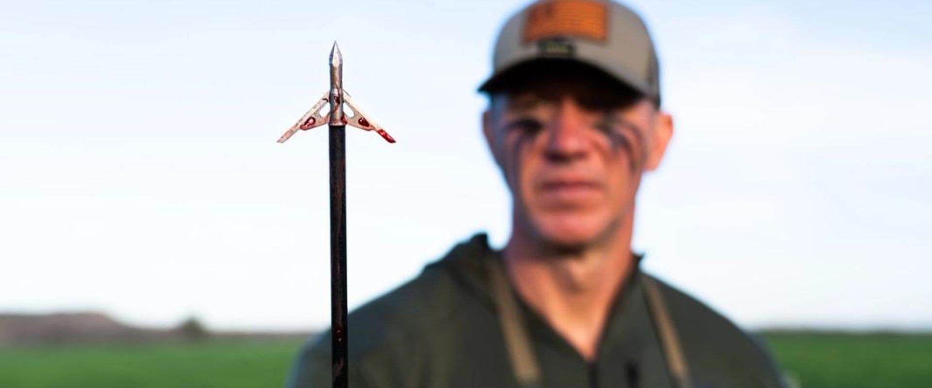 John Dudley blurred behind an arrow in focus, shooting a compound bow concept.