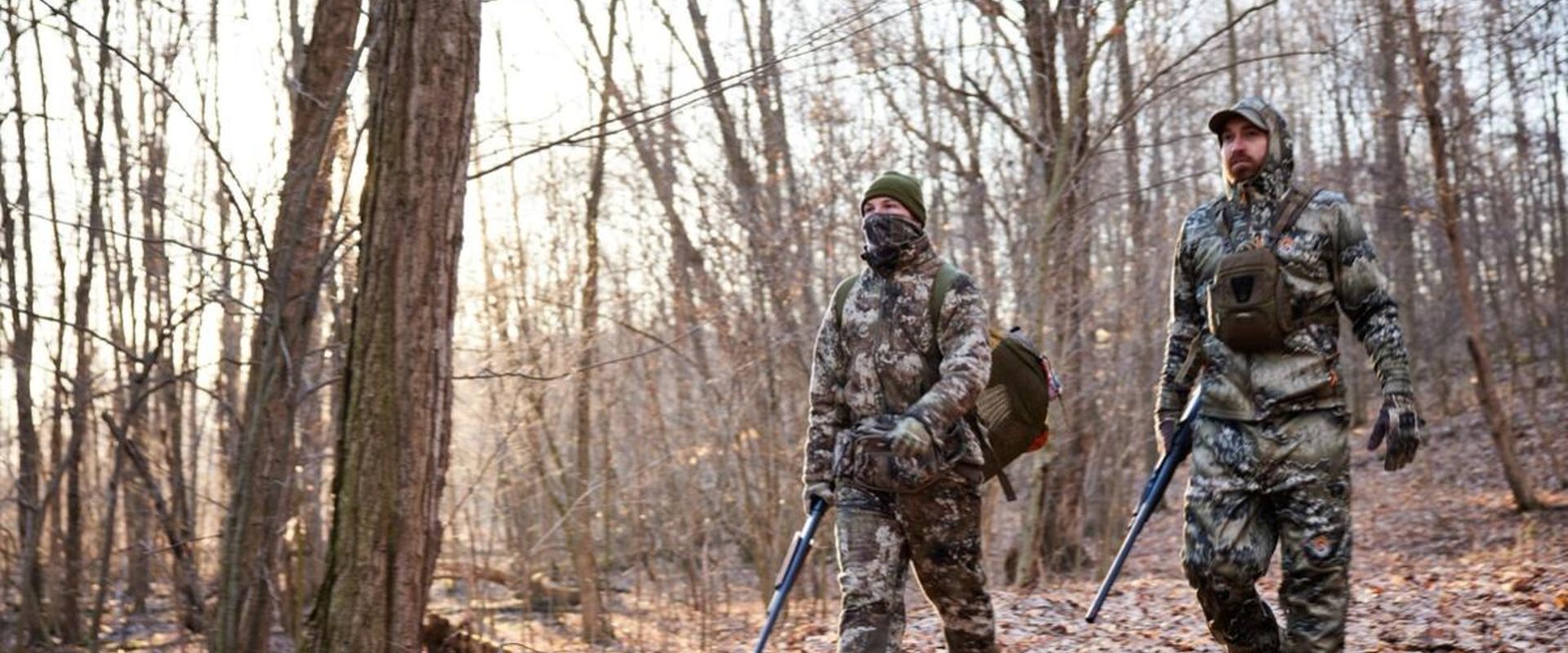 Two hunters in turkey gear walk through the woods, hunt Merriam turkey concept.