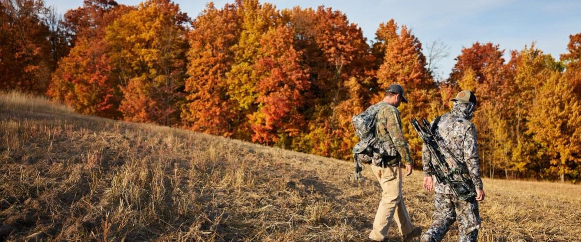 Two hunters walking in field near trees, how to find walk-in hunting in Iowa concept. 