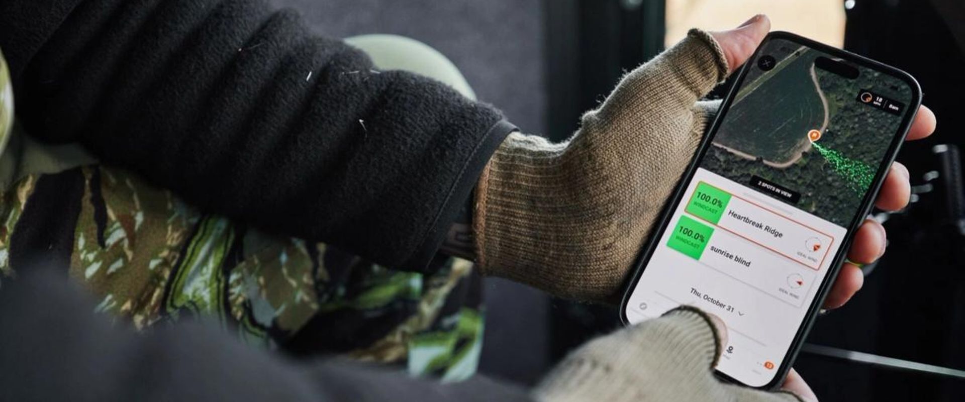 Close-up of hands holding a phone showing the HuntWise hunting weather app on screen.