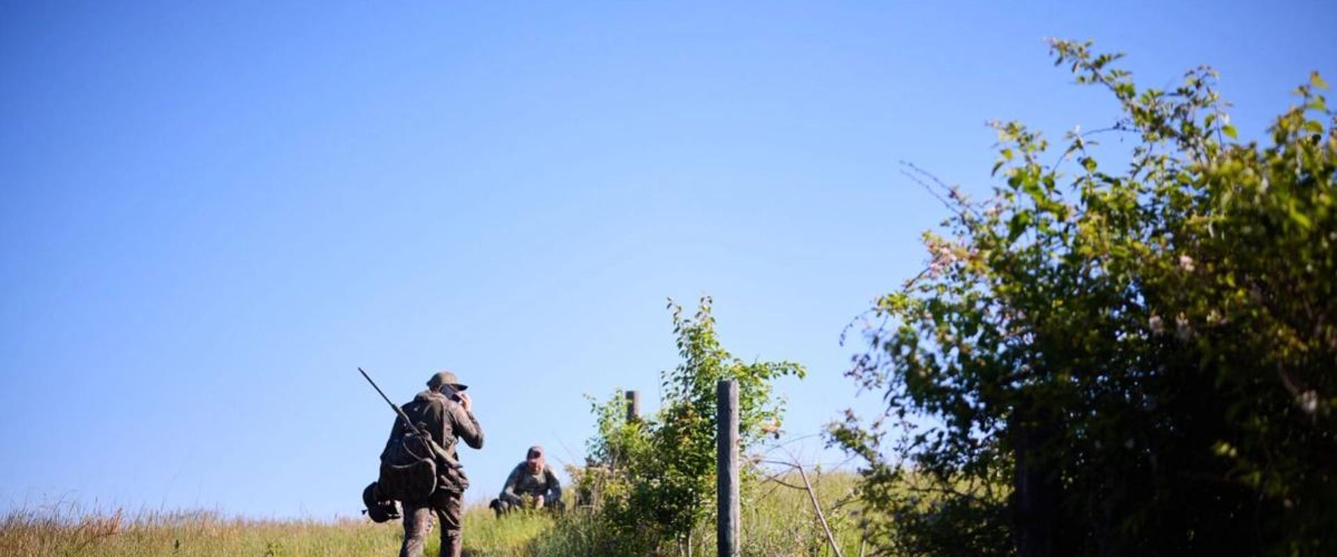 Two hunters near fence in field, walk-in hunting programs concept.