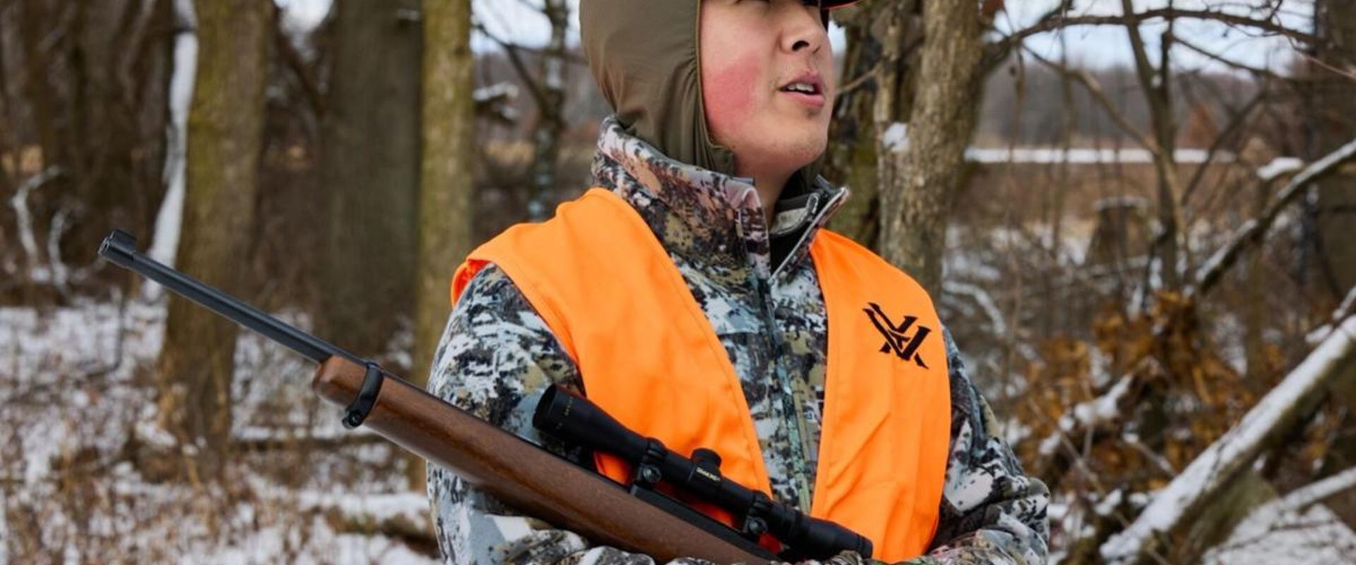 Hunter in blaze orange with rifle, best caliber for small game concept.