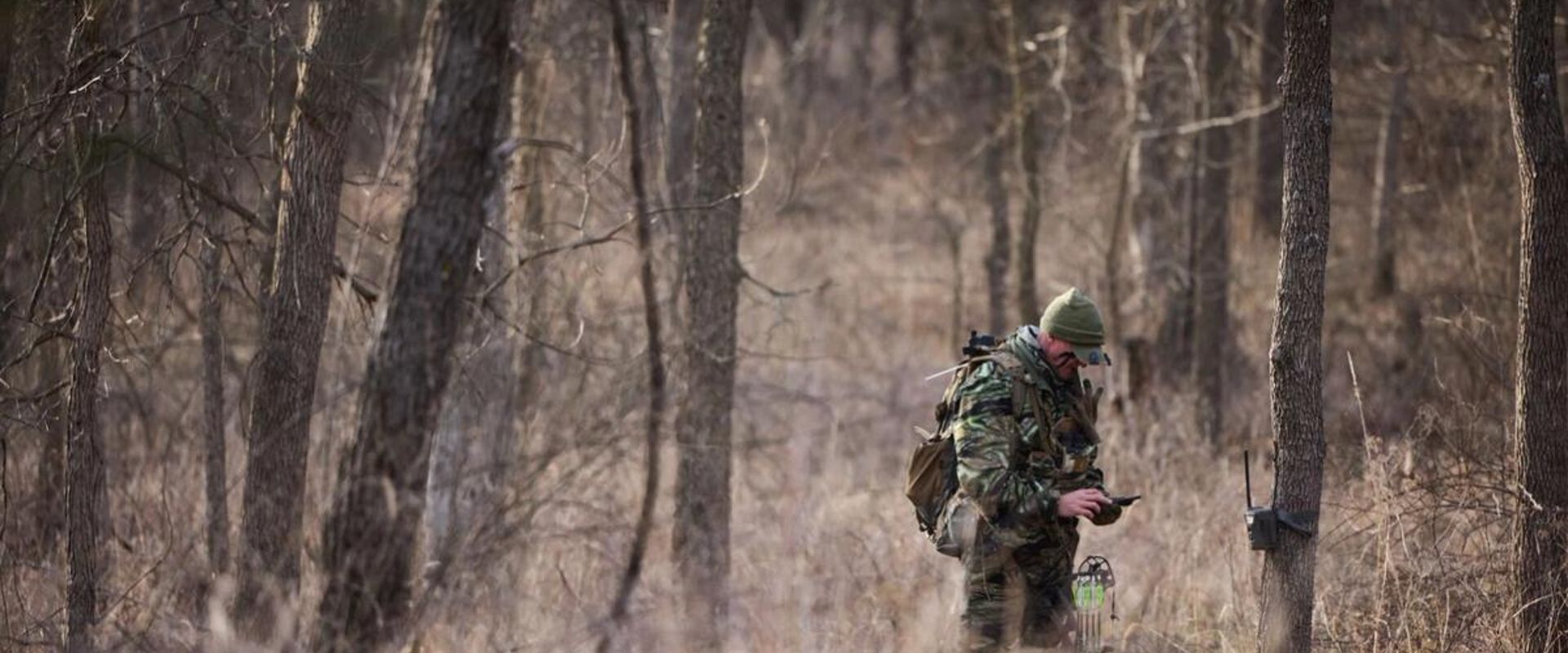 Hunter John Dudley checks phone and trail cam in woods, look for deer hunting land concept.