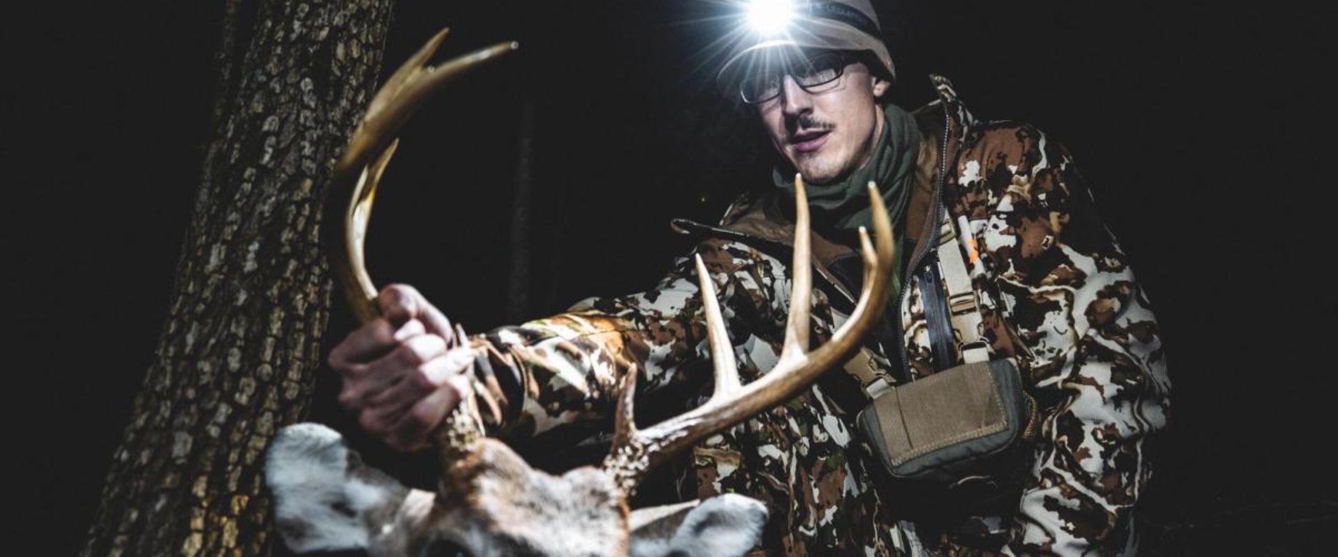 A hunter wearing a head lamp holds up a deer's antlers and head after a hunt, HuntWise app concept.