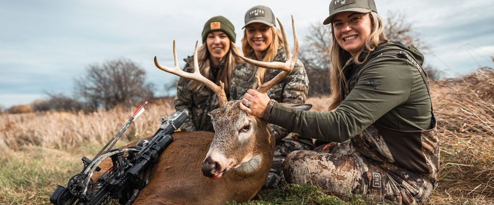 Three women in camo pose with a deer after a kill, find the best hunting time with HuntCast concept.