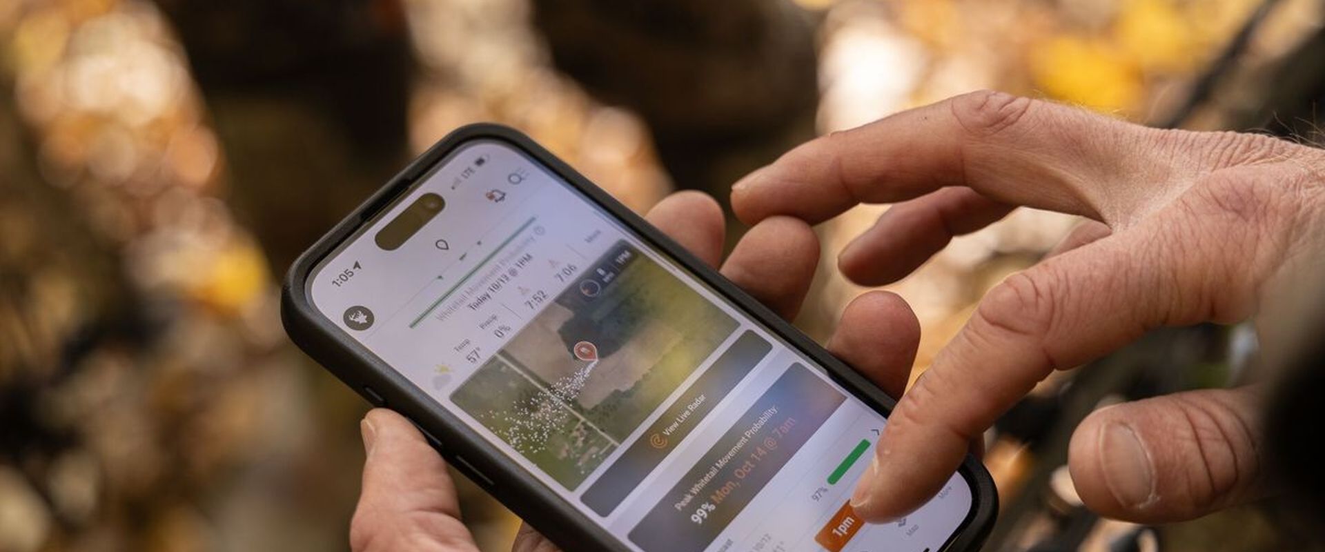 Close-up of a hunter's hands holding a phone and using the HuntWise hunting app.