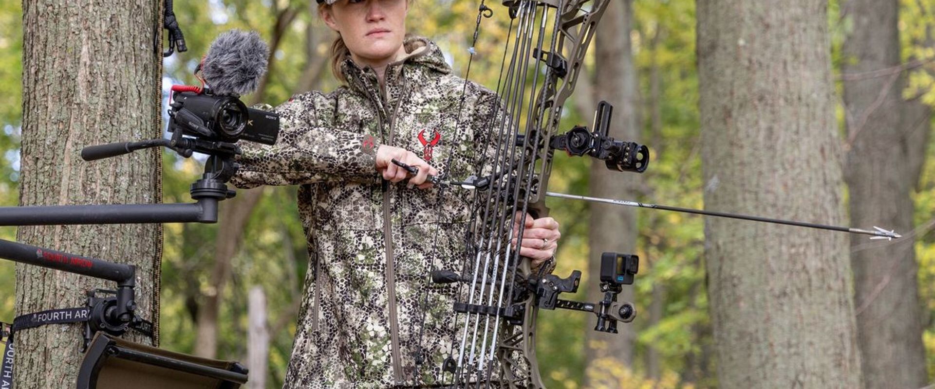 A female hunter in a tree stand gets ready to aim a bow, gun vs. bow shot placement concept.