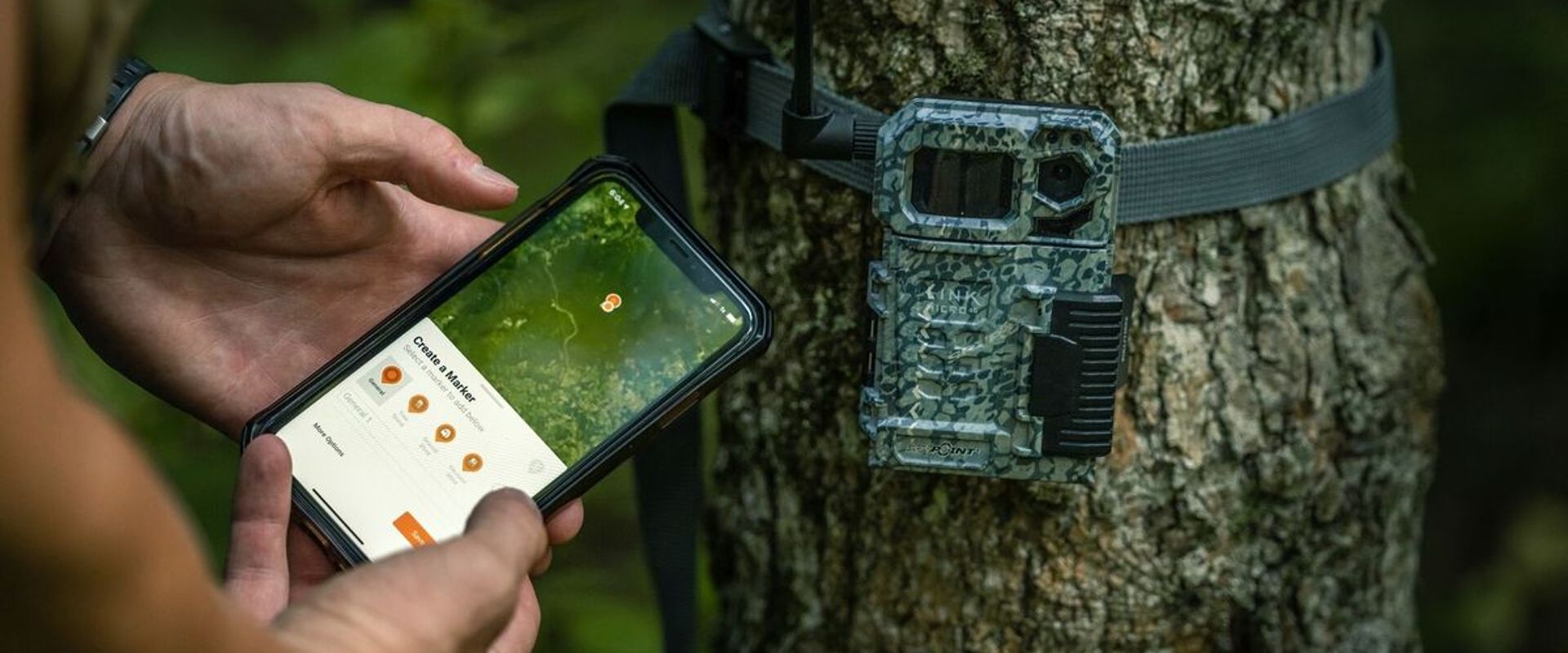 A trail cam on a tree and hunter using HuntWise app, deer hunting off season prep concept.