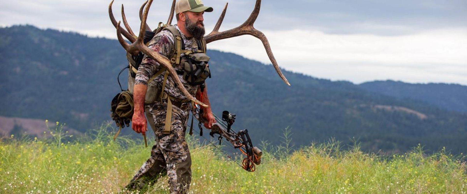 A hunter walks on a ridge carrying a large set of antlers, HuntWise pros concept.