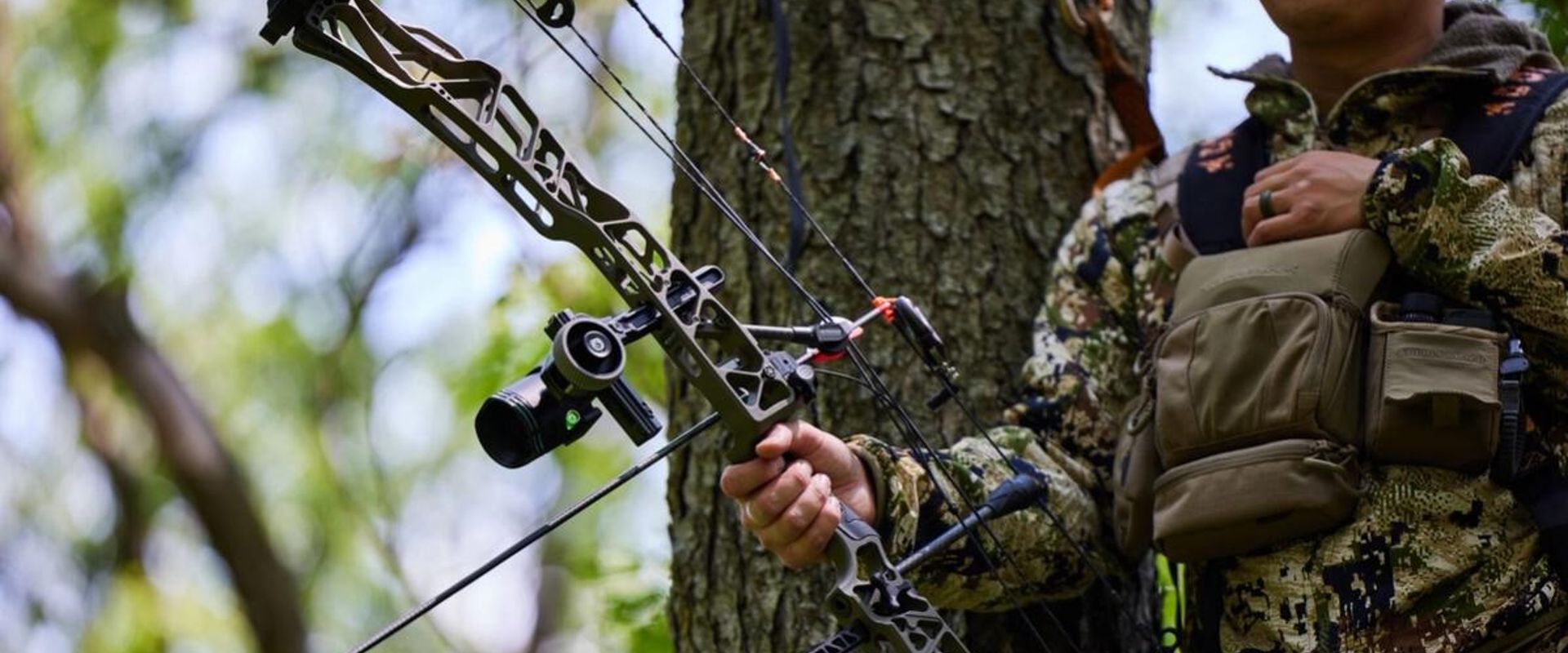 A hunter in camo in a tree stand with a bow, ready for Indiana deer season concept.