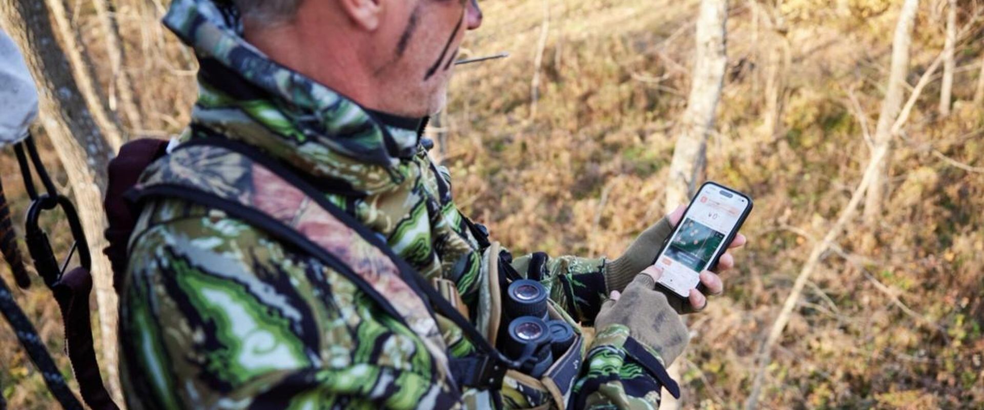 A hunter looks at a phone in the field, best wind direction app for hunting concept.
