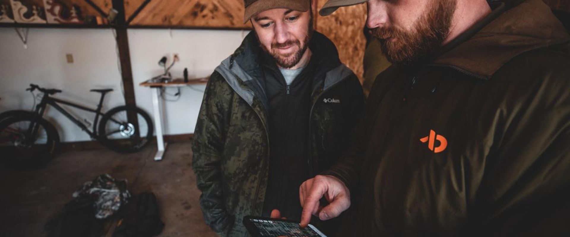 Two hunters looking at a phone, share nearby hunt areas concept.