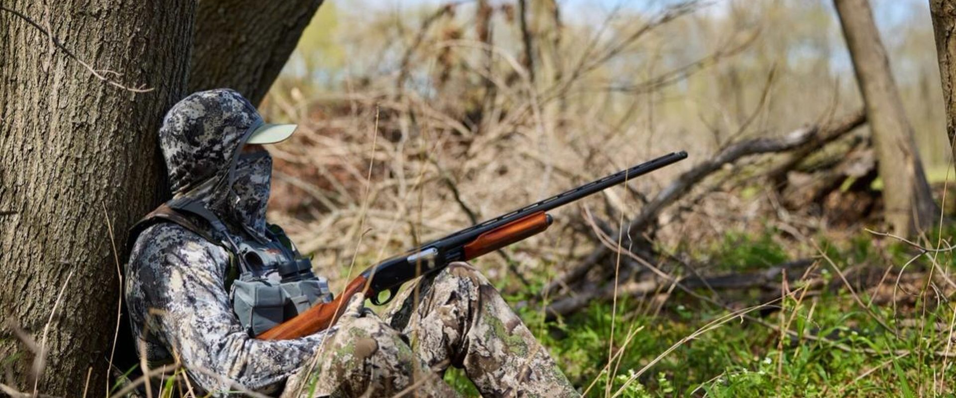 Hunter in camo against tree with shotgun, 12-gauge vs 20-gauge concept.