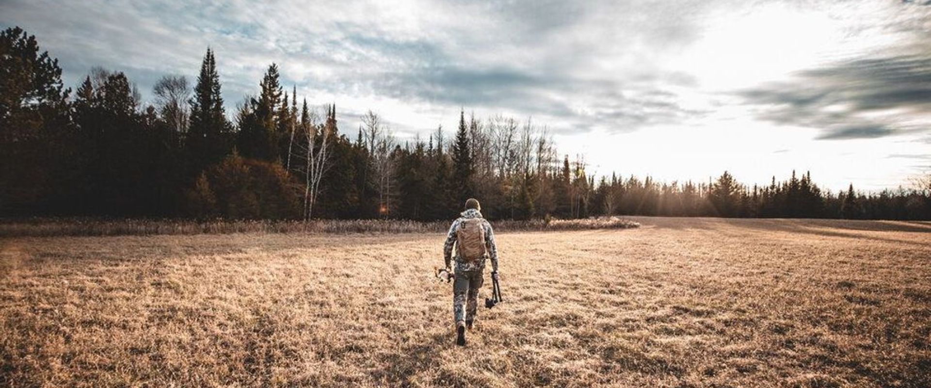 A hunter walks across a field with hunting gear, understanding deer movement concept.