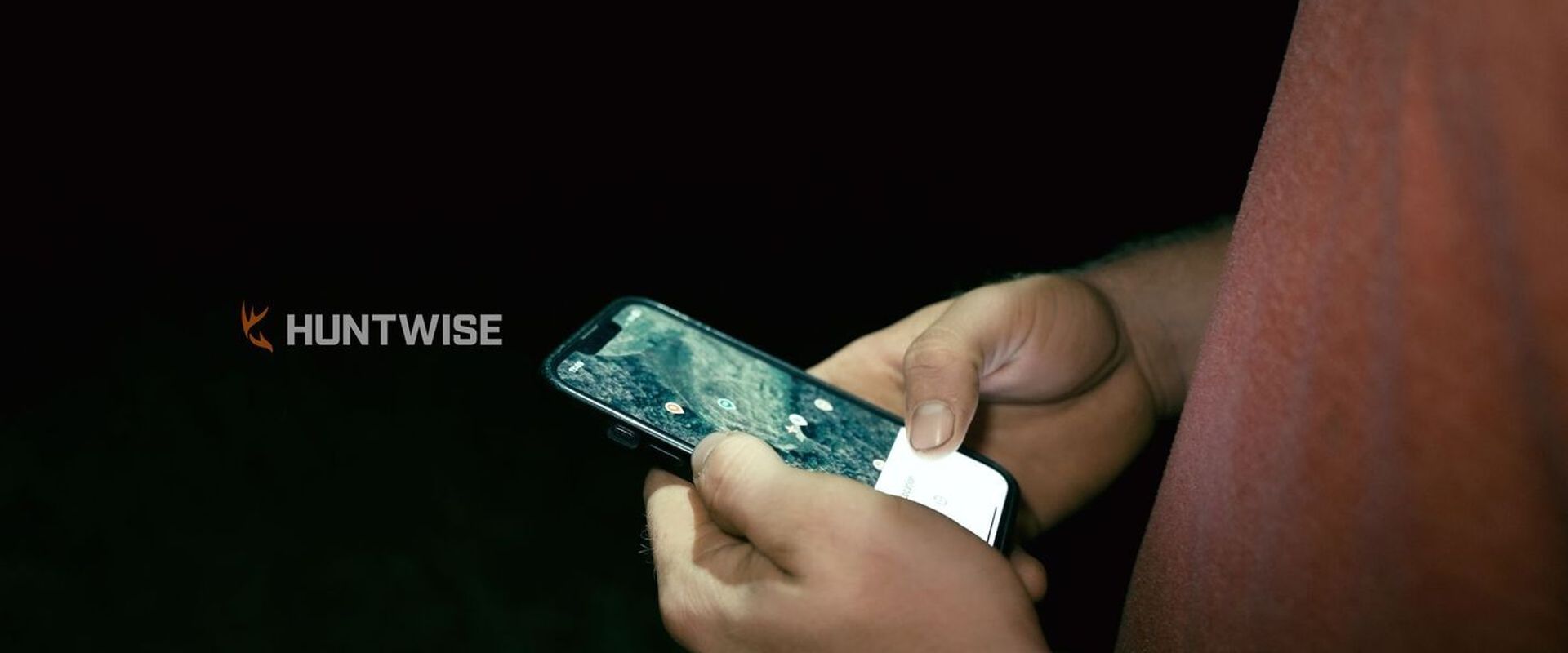 Close-up of hands holding phone showing hunting app with HuntWise logo.
