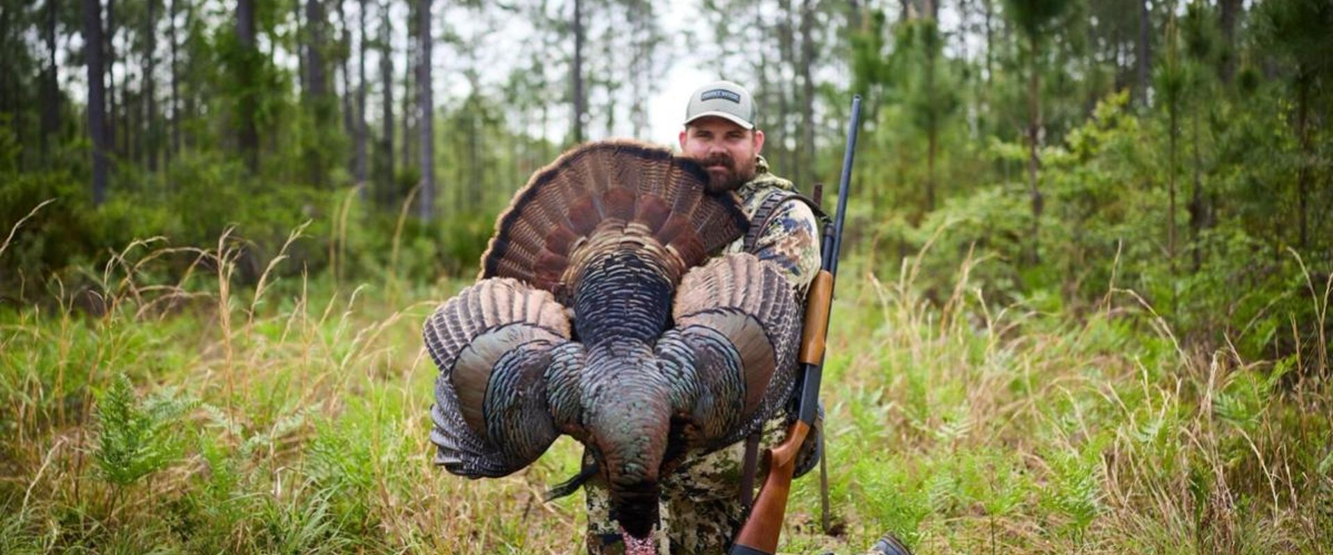 Hunter kneels with turkey after hunt, best caliber for turkey hunting concept.