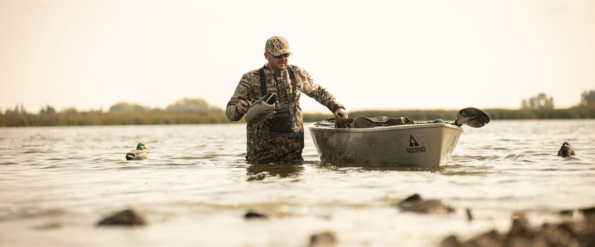 Hunter in waders in the water with canoe setting decoys, best duck hunting equipment concept.