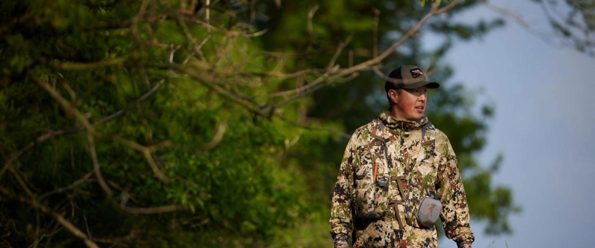 Hunter in camo with firearm walks near trees, how to find walk-in hunting in Kansas concept. 