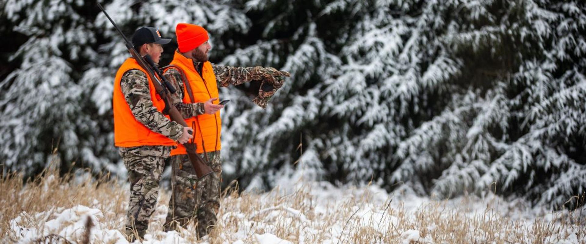 Two hunters in blaze orange look into snowy trees, late-season whitetail hunting concept.