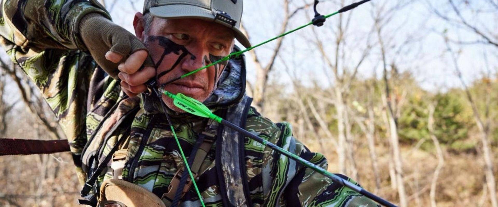 John Dudley wears a HuntWise hat and draws an arrow, how to get better at archery concept.