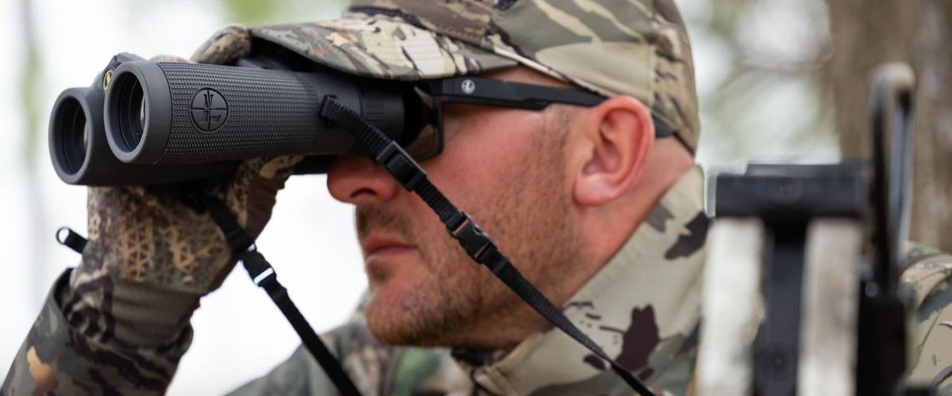 A hunter in camo uses binoculars, choosing lightweight hunting clothes concept.
