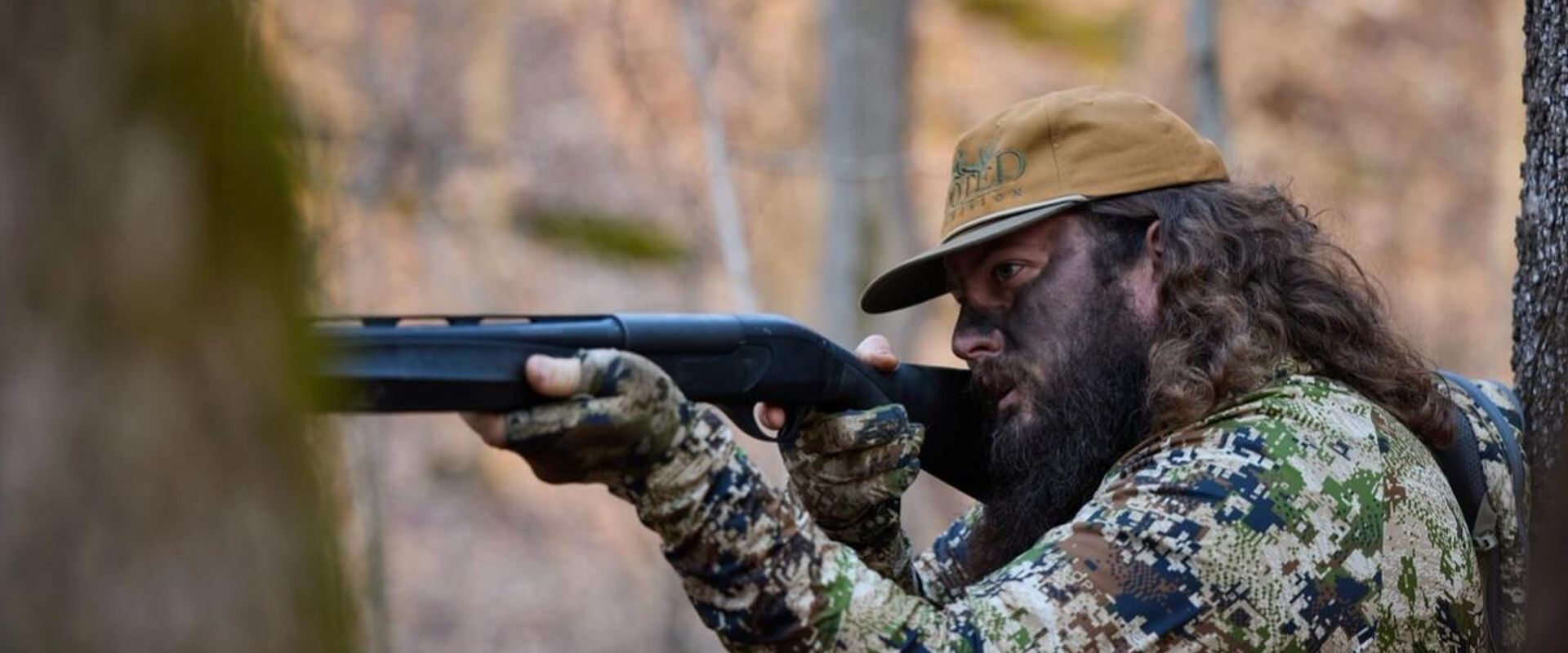 Ben Cole of RootedTV aims a shotgun in the woods, spring hunting concept.