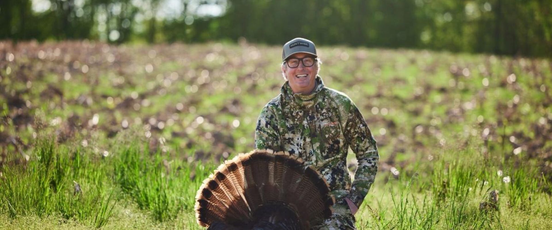 A hunter smiles and poses with a turkey after a successful hunt.
