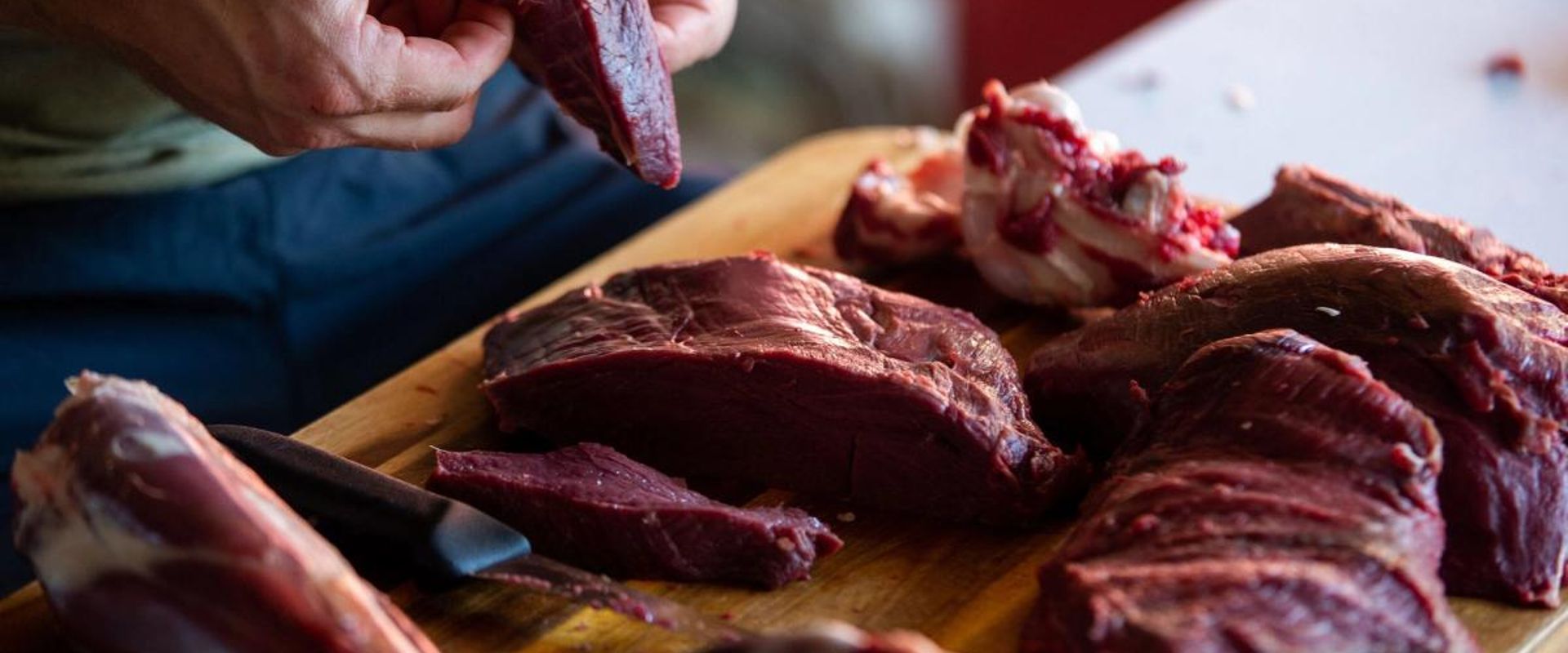 A person handling venison meat on a cutting board, venison dishes concept.