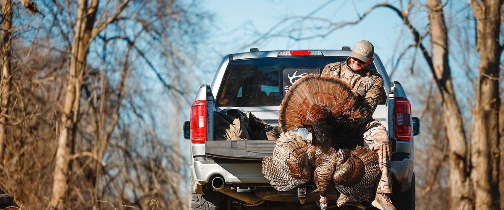 A hunter sits on a truck tailgate holding a wild turkey after a hunt, turkey species concept.