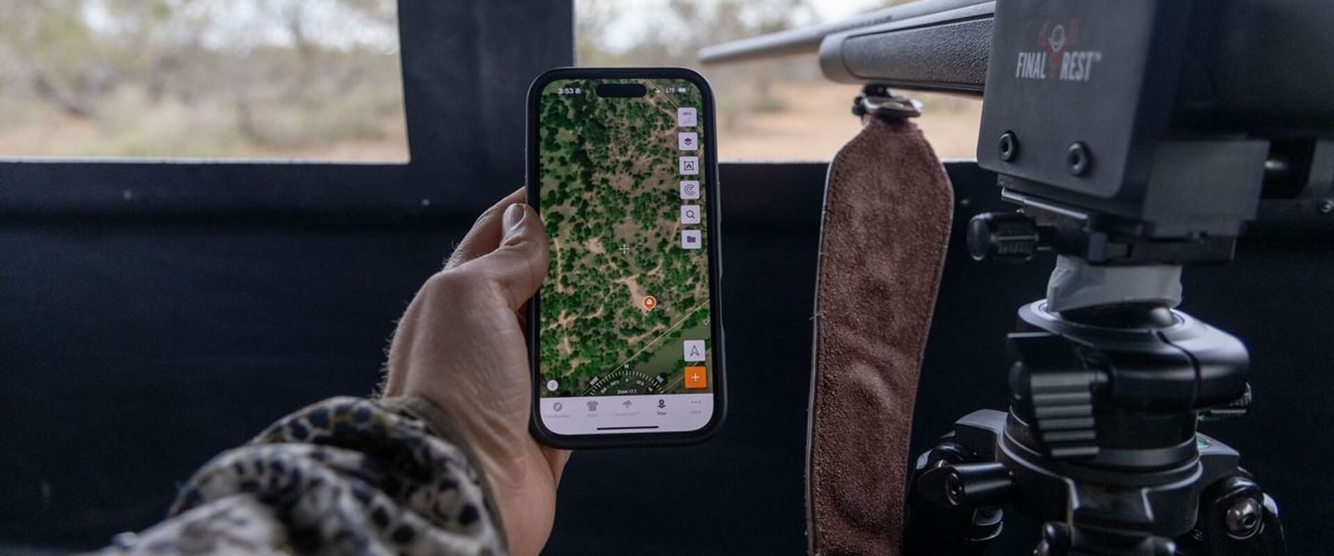 Hunter holds phone showing Huntwise next to rifle in blind, where can I hunt concept.