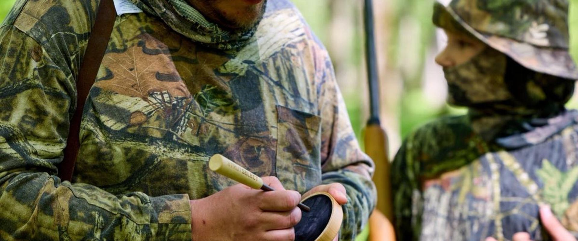 Hunter using turkey call with boy, best turkey hunting gear concept.