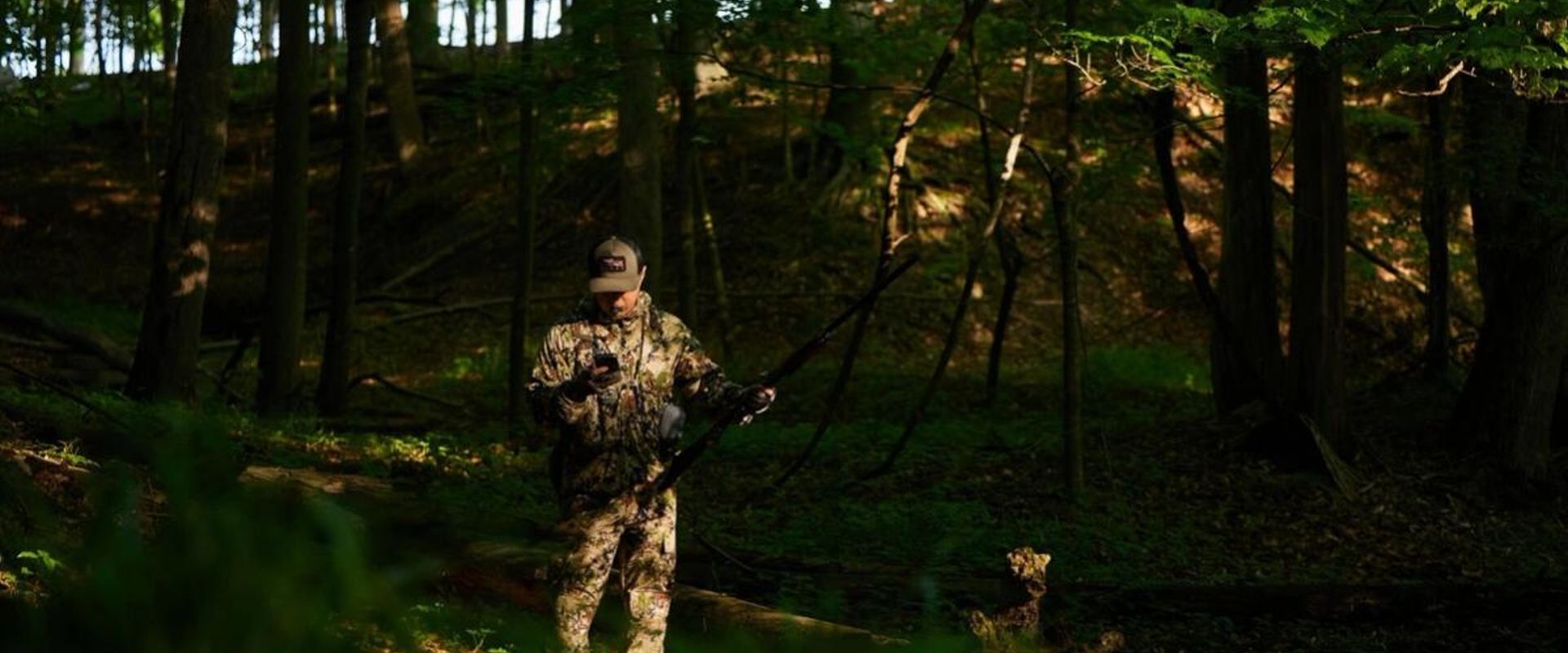 A hunter in the woods looking at a phone, how to find public hunting land near me concept.