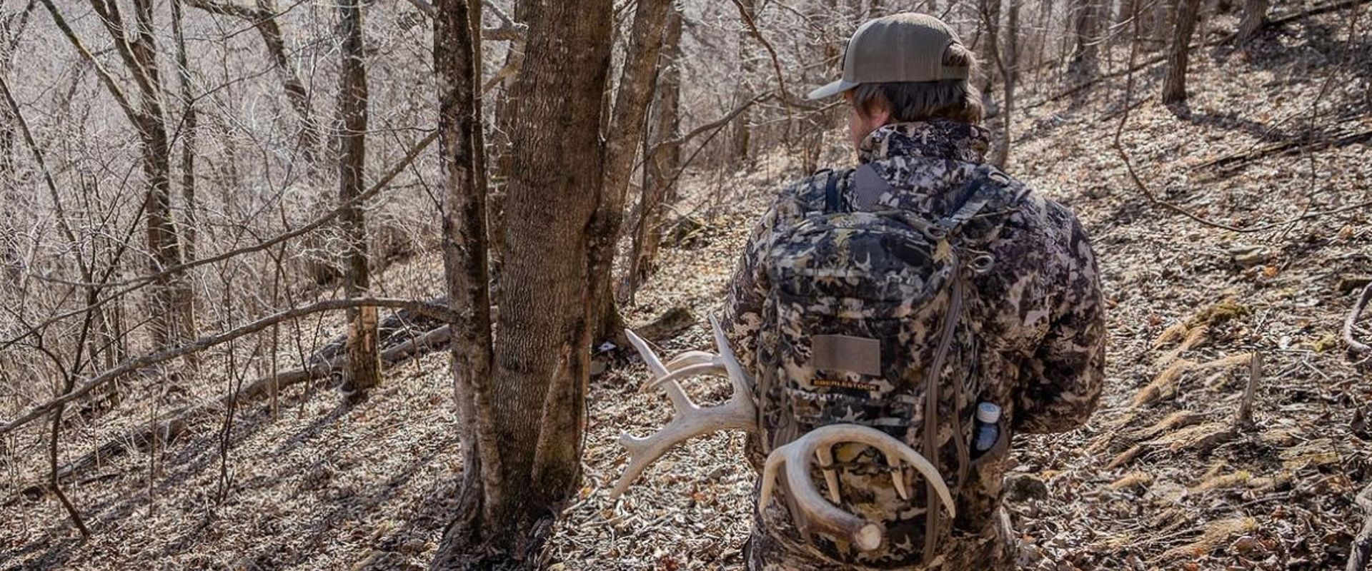 A hunter in the woods wearing a pack with shed antlers attached.