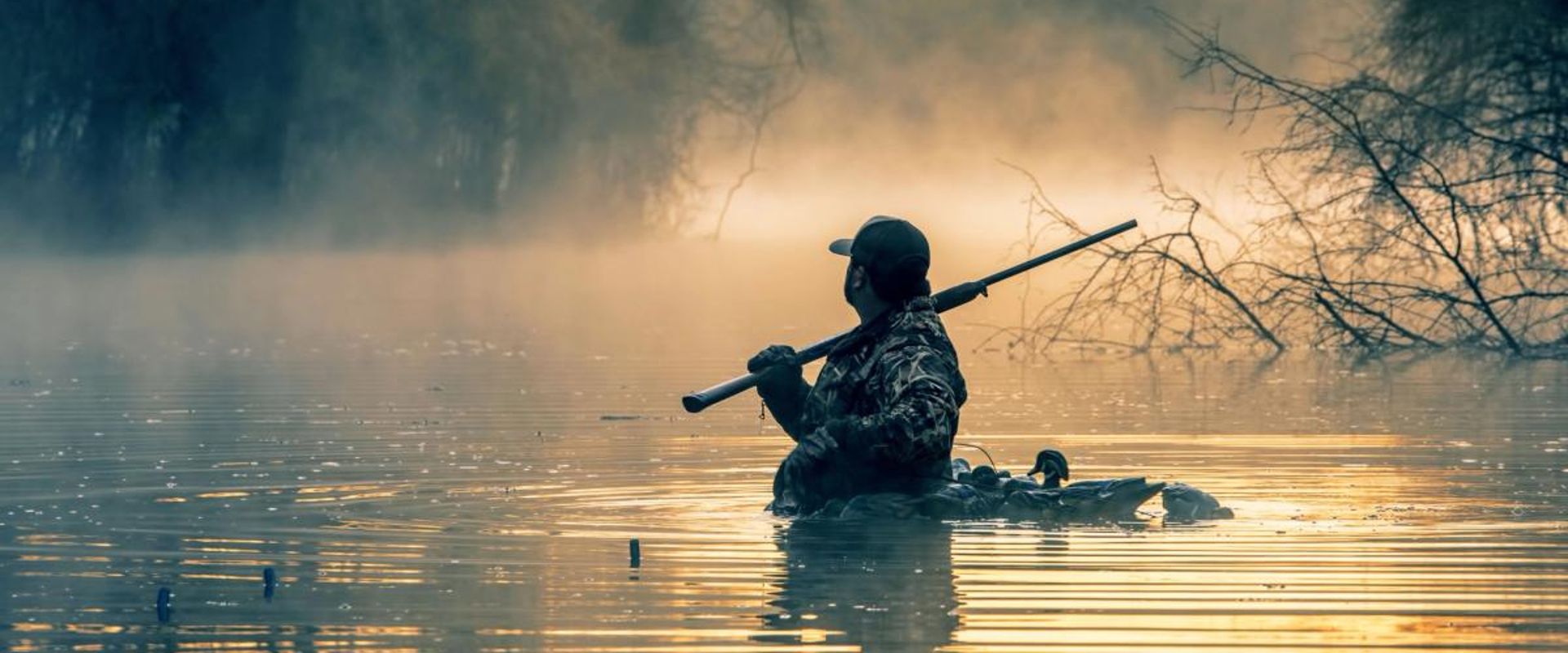 A hunter in the water with a shotgun and waterfowl decoys, best decoys concept.