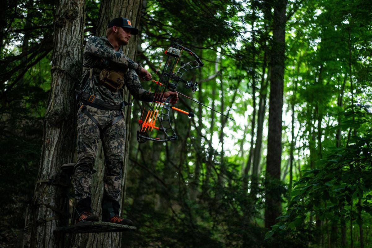 A hunter with a bow wearing camo while in a tree stand, hunt big bucks in thickets concept.