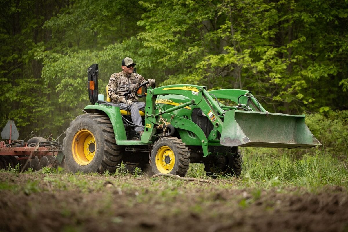 A hunter uses a tractor to clear land, when to plan spring food plots for deer concept.