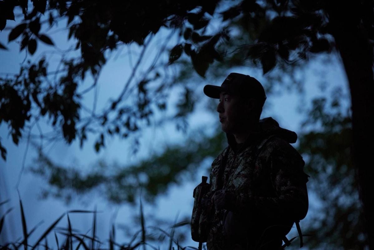 A hunter stands near a tree in the dark, night hunting concept.