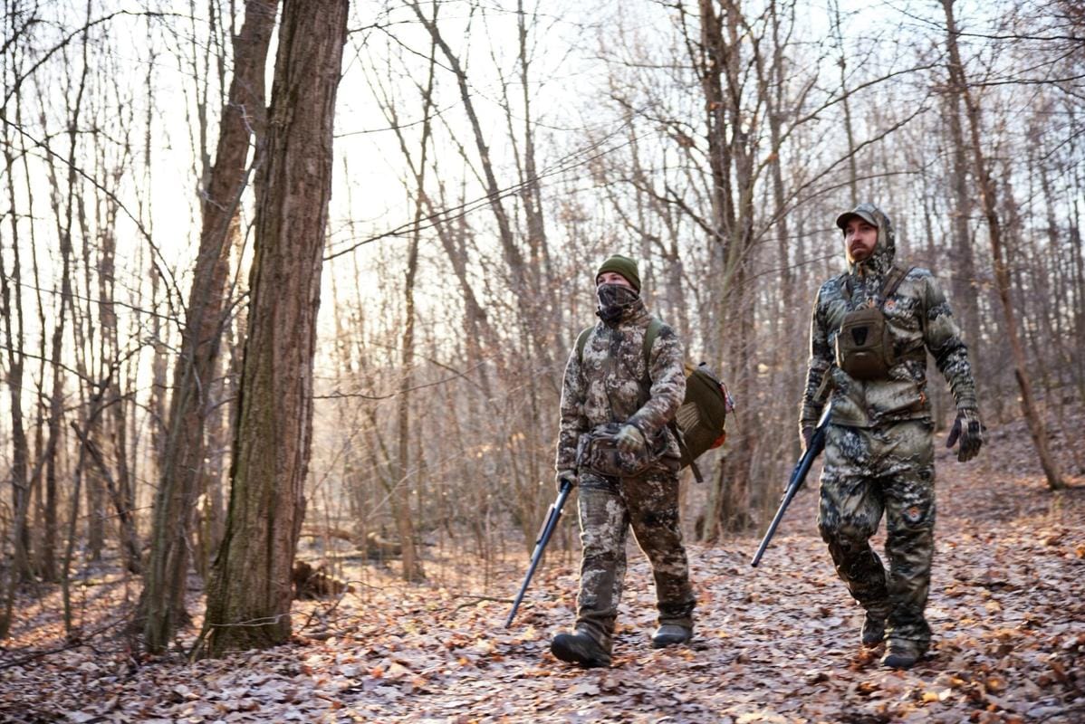 Two hunters in turkey gear walk through the woods, hunt Merriam turkey concept.