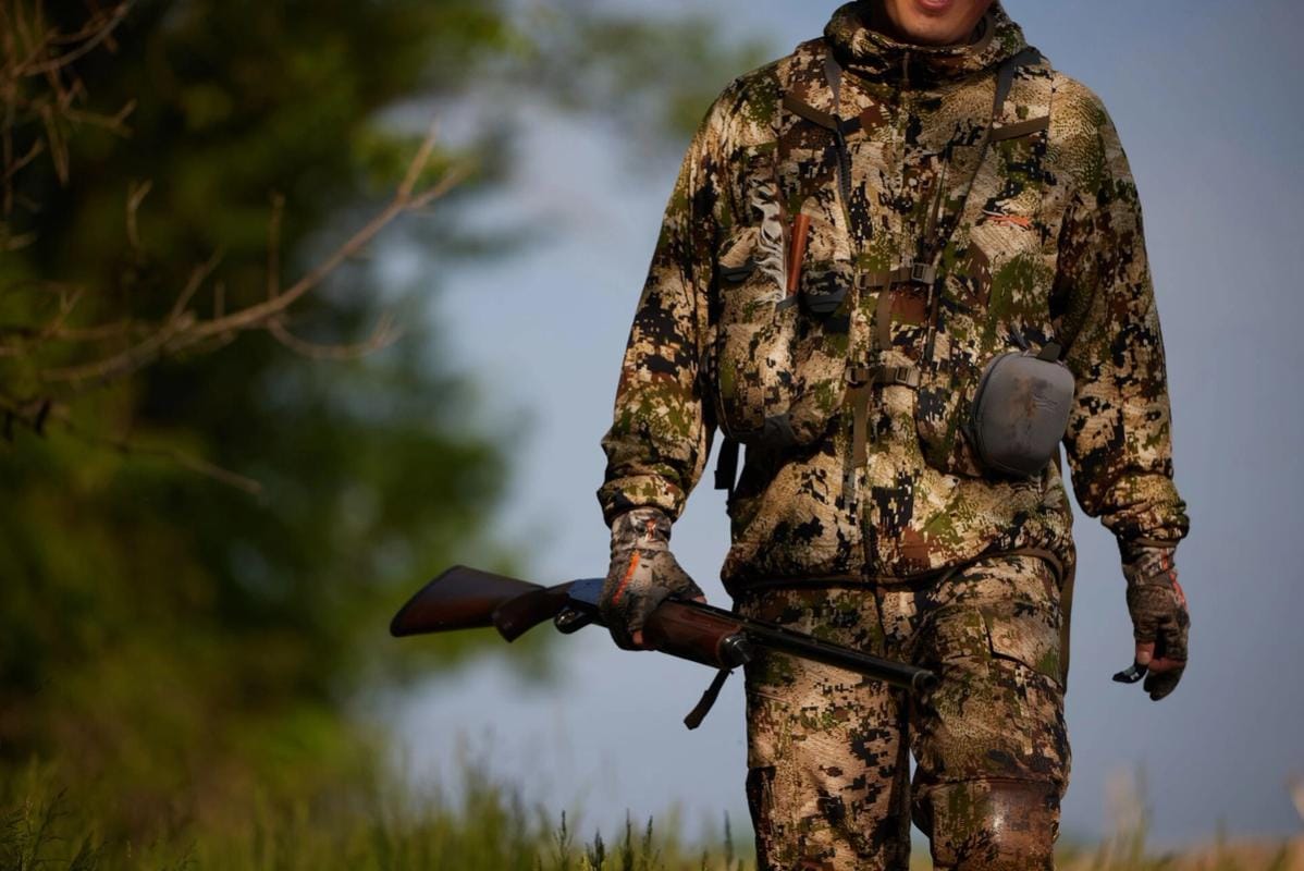 A hunter in camo holding a rifle in the field, get a Mississippi hunting license concept.
