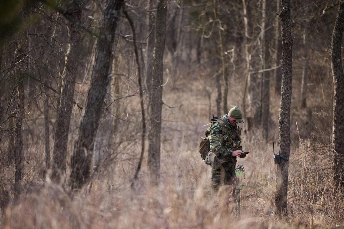 Hunter John Dudley checks phone and trail cam in woods, look for deer hunting land concept.