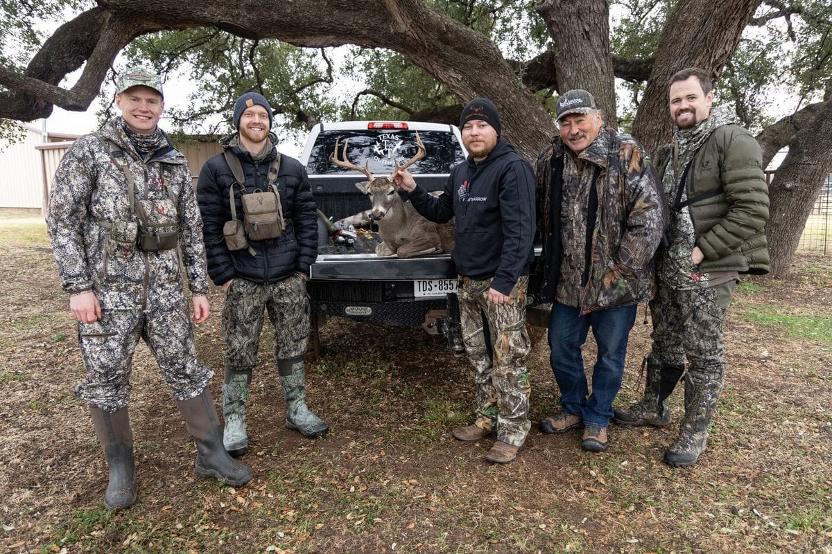 Several hunters gather around a buck in the back of a truck after a hunt.