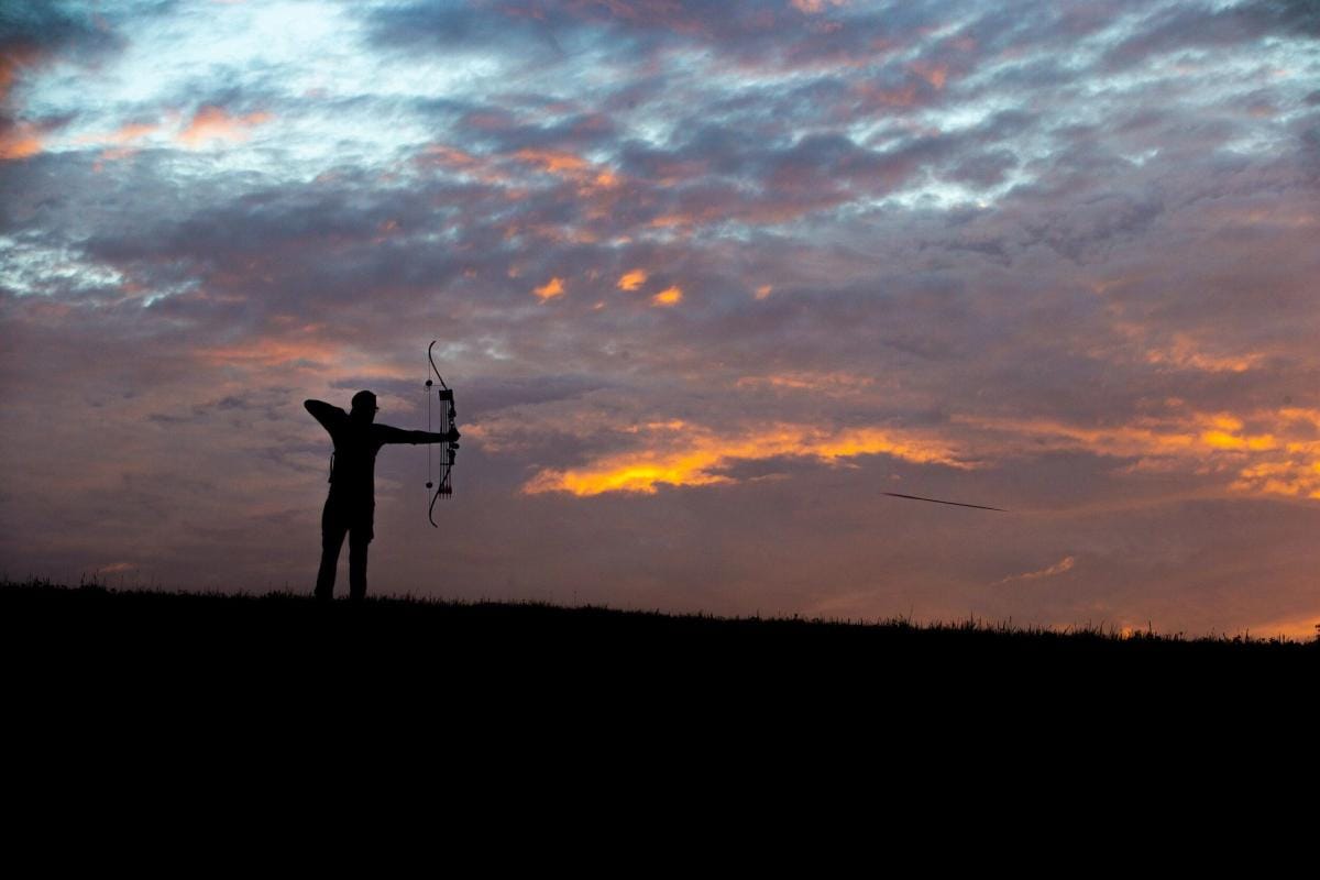 A bowhunter in the distance draws the bow, hunting whitetail deer concept.