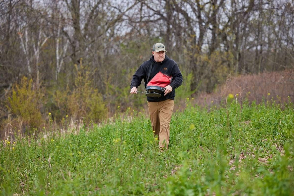 Jeff Sturgis with a seed spreader walks through a food plot, what do deer eat concept.