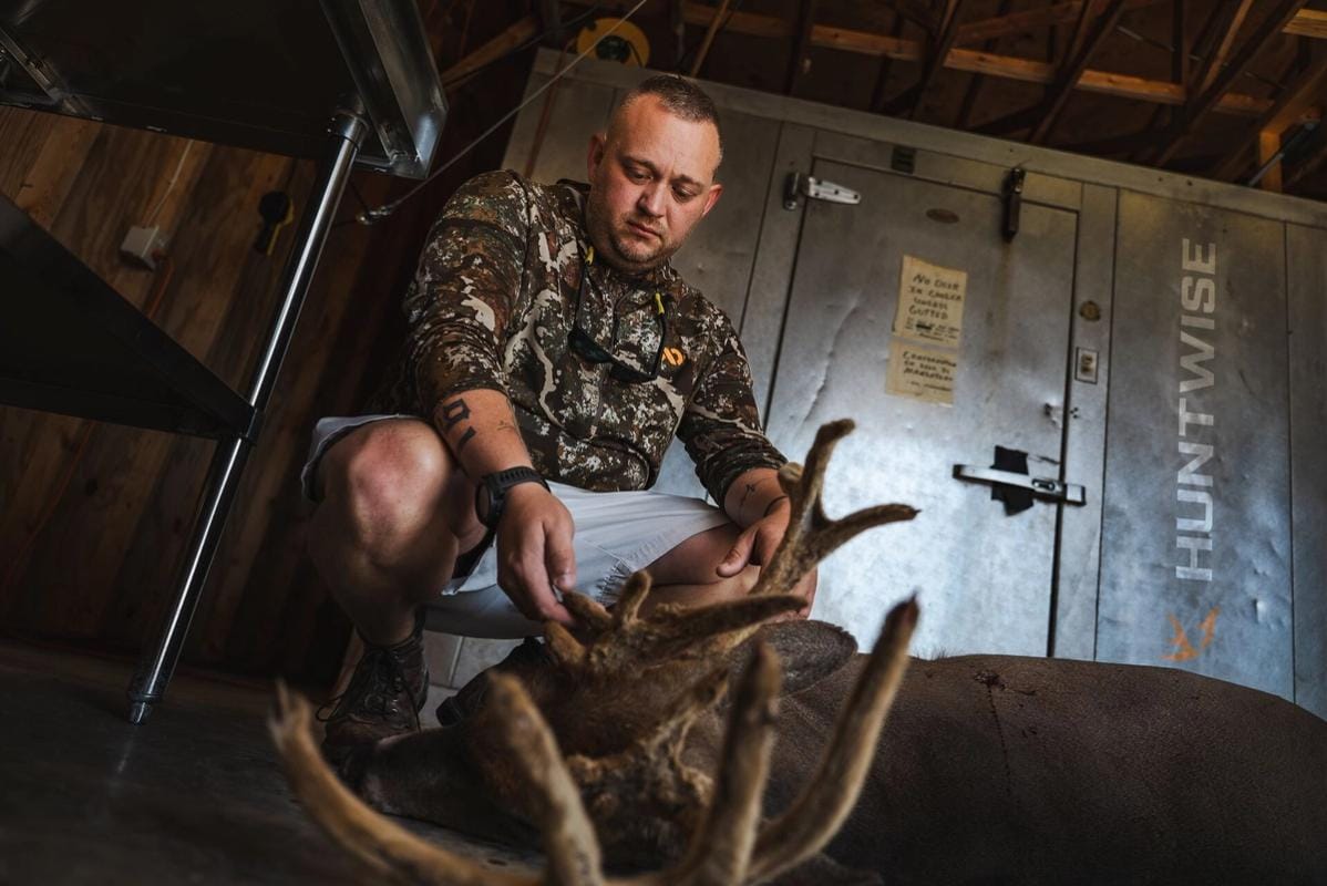 Hunter with buck deer after hunt in front of cooler, hunting whitetail before the rut concept.