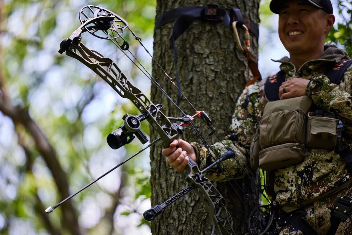 A hunter in camo in a tree stand with a bow, ready for Indiana deer season concept.