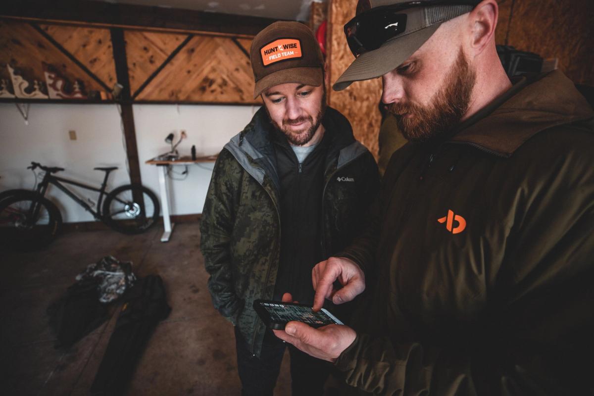Two hunters looking at a phone, share nearby hunt areas concept.