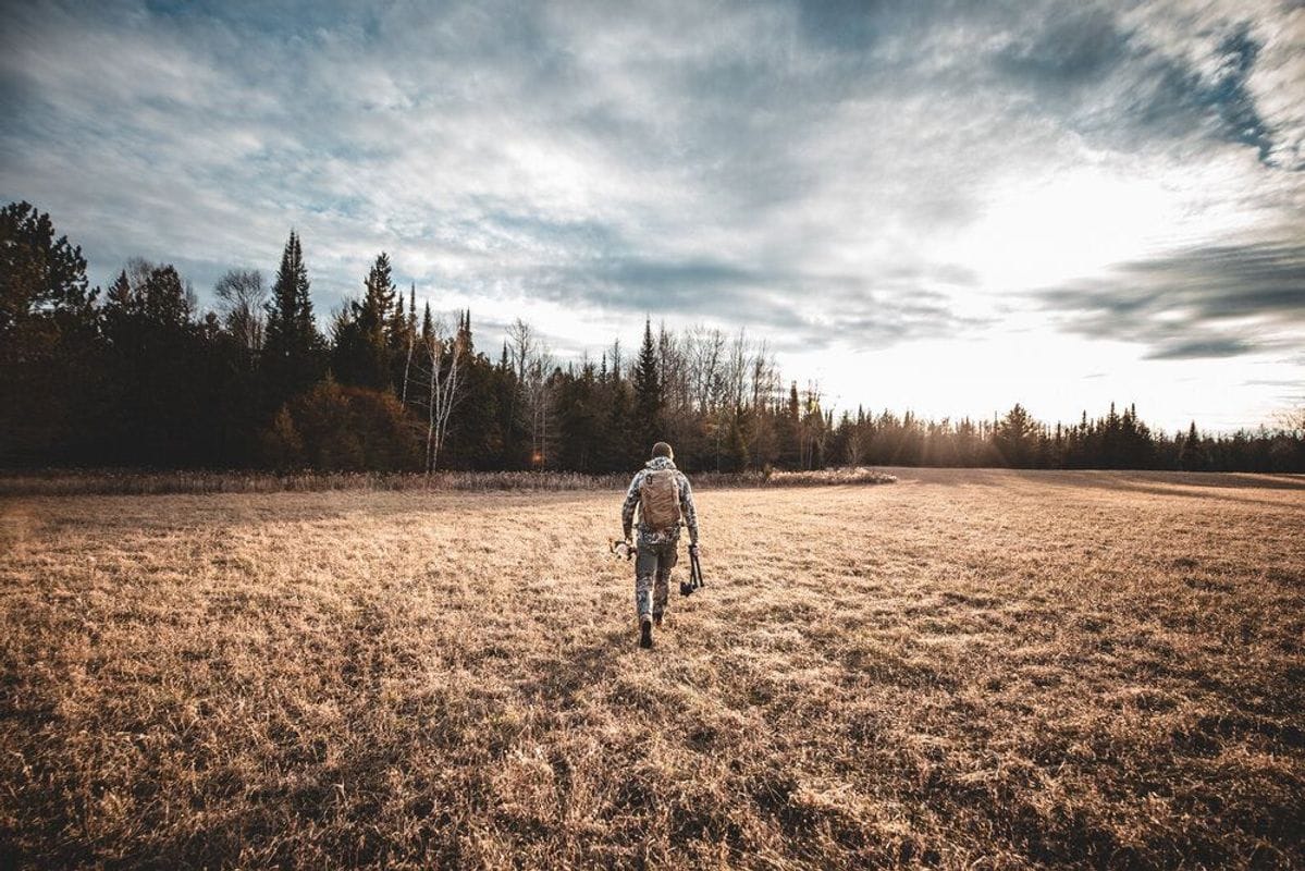 A hunter walks across a field with hunting gear, understanding deer movement concept.